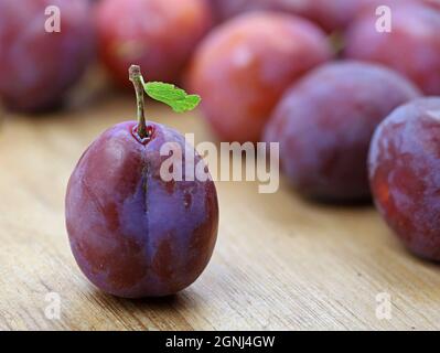 Fresh purple plum with green leaf on wooden table with plums in background Stock Photo