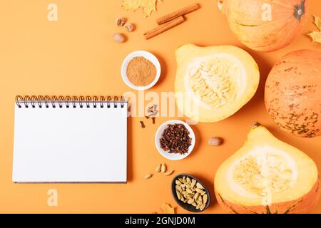 Blank notepad template next to pumpkins, spices and autumn leaves on orange background, flat lay. Stock Photo