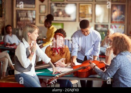 Group of young creative people in a pleasant atmosphere in the office are enjoying a process of designing a new guitar Stock Photo
