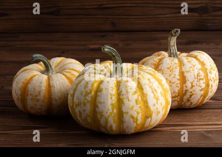 Three striped yellow pumpkins on dark wooden background, Halloween or Thanksgiving concept Stock Photo