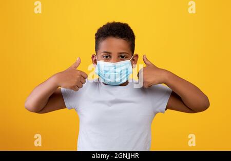 Funny black boy wearing protective face mask, showing thumb ups Stock Photo