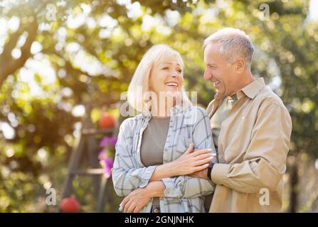 Loving retired spouses enjoying time together in park, walking at sunny autumn day, man embracing her wife, free space Stock Photo