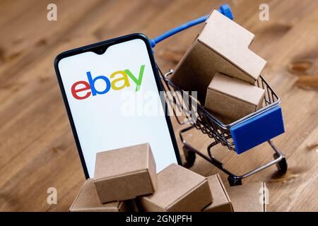 Smartphone with eBay logo on the screen, shopping cart and parcels. Stock Photo
