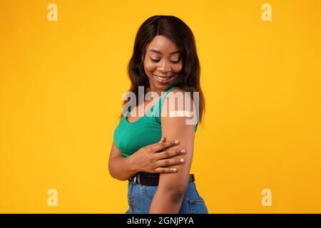 African American Woman Vaccinated Against Covid-19 Showing Arm, Yellow Background Stock Photo