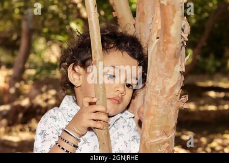 Close-up portrait of An Indian resident little hindu boy posing to think sadly and unhappy with laying head on tree trunk Stock Photo