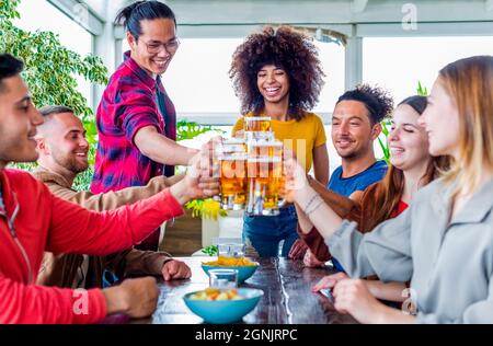 happy group of diverse friends celebrating together on a table in a bar restaurant indoors making celebratoty toast with beers during happy hour Stock Photo