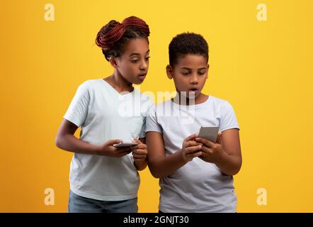 Shocked black brother and sister using smartphones Stock Photo