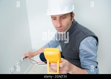 electrician testing plug socket with multimeter Stock Photo