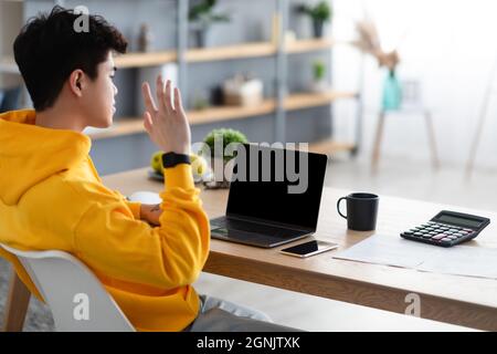 Rear view of asian man working on laptop waving hand Stock Photo