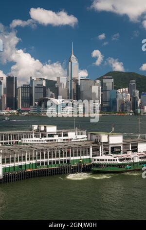 A Star Ferry arrives at Tsim Sha Tsui pier in Kowloon, with Wan Chai, Hong Kong Island, visible across Victoria Harbour Stock Photo