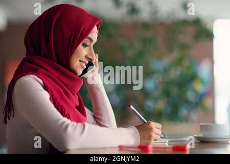 Side view of muslim woman talking on cellphone at cafe Stock Photo