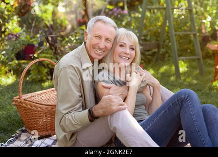 Portrait of senior couple sitting in garden and hugging, having picnic outdoors and smiling to camera Stock Photo