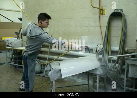 Worker spraying white paint with a pulverizer on the metal part of the body plane. February 3, 2020. Kiev, Ukraine Stock Photo
