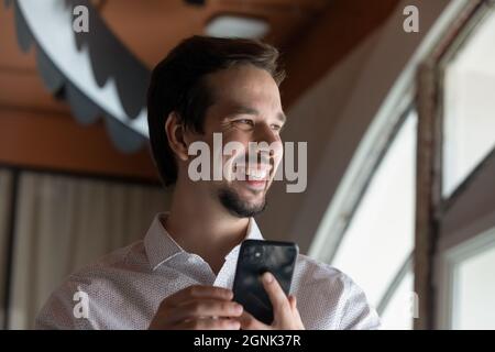 Happy millennial guy using smartphone, holding cell Stock Photo