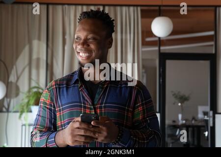 Happy millennial Black hipster employee holding mobile phone Stock Photo