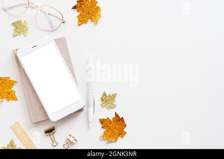 Autumn style workspace with smartphone mockup, glasses, maple leaves decor on white background. Feminine home office desk table. Flat lay, top view. Stock Photo