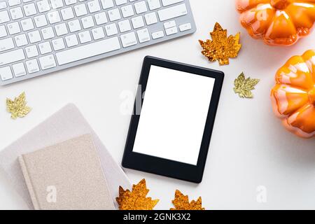 Autumn composition. Feminine desk table with pumpkins, tablet ebook with blank screen, keyboard, fall leaves on white background. Flat lay, top view. Stock Photo