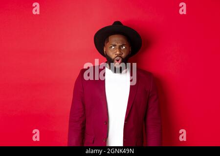 Fashion and party concept. Shocked and displeased black man staring at something unpleasant, looking upper left corner and frowning, standing against Stock Photo