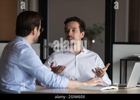 Two office employees meeting and working at workplace laptop, talking Stock Photo