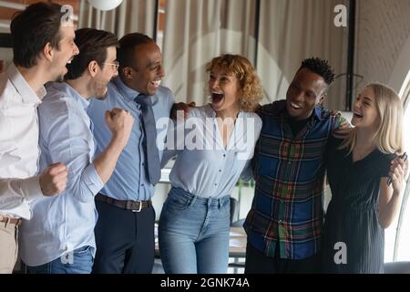 Group of happy excited diverse employees hugging, shouting for joy Stock Photo