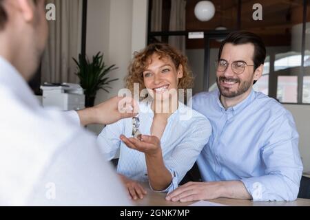 Real estate agent giving key to happy family couple of customers Stock Photo