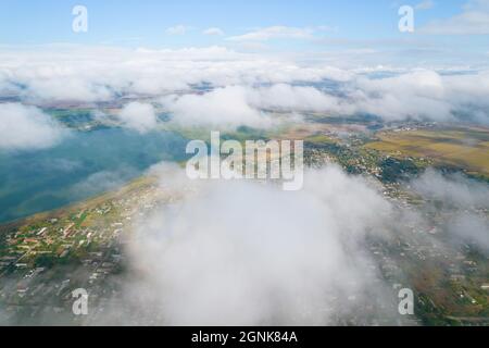 Cumulus clouds, aerial background. Aerial shot with top view of white fluffy clouds gathering. In between the clouds the ground is visible here and th Stock Photo