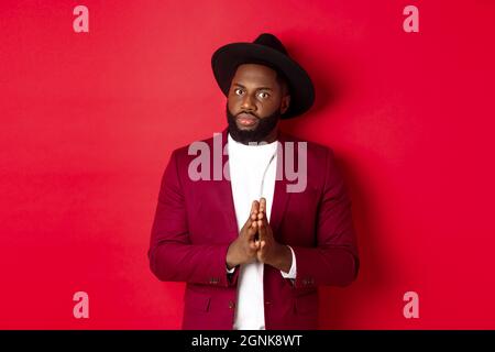 Serious looking man getting ready to business, holding hands pressed together and nervously staring at camera, listening closely, standing against red Stock Photo