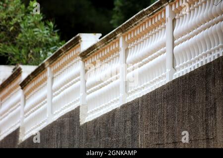 Long row of balcony fence made of vintage retro looking newly painted white balusters covered with dirty old wide guardrail on top of dark grey Stock Photo