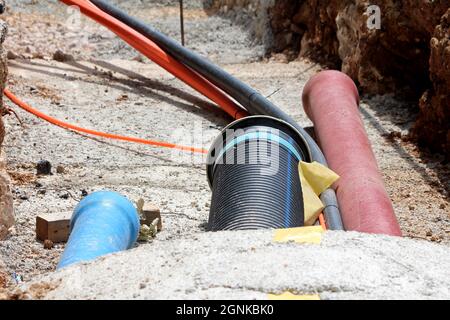 Two blue and light red metal and one black corrugated PVC PE plastic pipes mixed with smaller diameter pipes at local construction site on top of Stock Photo