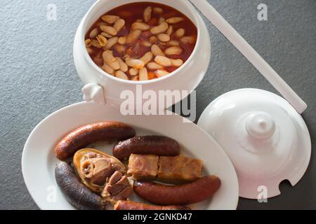 Tasty homemade asturian fabada; bowl with the beans and side dish with meat, jam, chorizo and blood sausages. Traditional gastronomy of Asturias, Spai Stock Photo