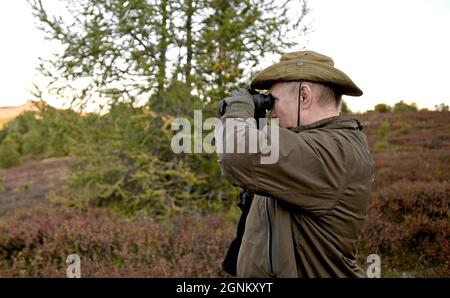 Siberia, Russia. 26th Sep, 2021. Russian President Vladimir Putin looks through a pair of binoculars during a short vacation with Defense Minister Sergei Shoigu to fish and hike early September shown in images released September 26, 2021 in the Siberian Federal District of Russia. Putin stopped over during a working visit to the Primorye and the Amur Region of the Russian Far East. Credit: Alexei Druzhinin/Kremlin Pool/Alamy Live News Stock Photo