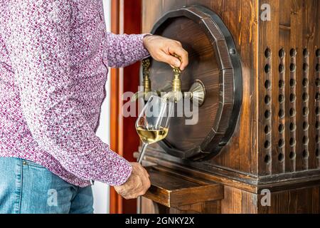 Person pouring wine from a wine barrel. Mature sommelier in winery basement pouring red wine into long-stemmed wine glass. Stock Photo