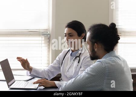 Smiling empathetic Indian practitioner showing laptop screen to male patient Stock Photo