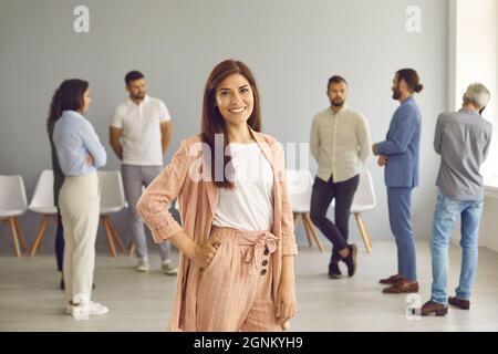 Portrait of successful and stylish young business woman standing on background of workspace. Stock Photo