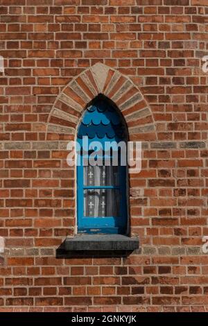 Blue arched window with decorative scales in red brick wall, Cornwall Stock Photo