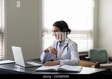 Happy young Indian general practitioner in headphones using laptop Stock Photo