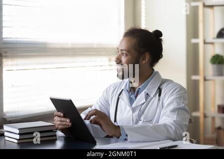 Happy millennial Afro American doctor looking at window away Stock Photo