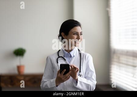Happy Indian GP doctor chatting online on mobile phone Stock Photo