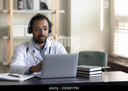 Serious GP doctor in headphones engaged in online virtual consultation Stock Photo