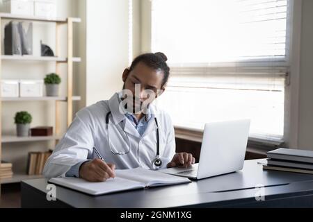 Serious focused GP doctor writing medical records at open laptop Stock Photo