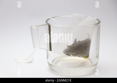 Glass tea cup with green tea bag, fresh herbs covered by very thin mesh bag placed inside cup on white background Stock Photo