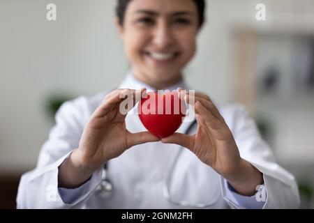 Smiling female cardiologist holding red heart, showing object at camera Stock Photo