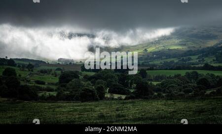 Dramatic storm clouds sweep across green Welsh valley landscape with rolling hills and farmland Stock Photo