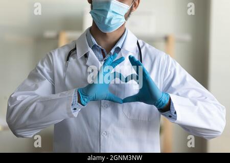 Young doctor in face mask, latex gloves showing finger heart Stock Photo