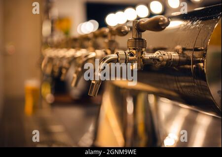 Draft beer taps in modern brewery, side view. Dark pub on a background. Stock Photo