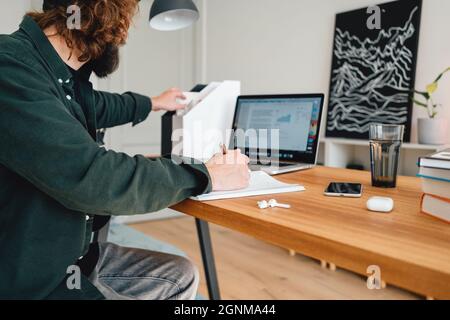 School student prepare for pass exam to university while digital learning. Pensive man at home while remote learning using laptop Stock Photo