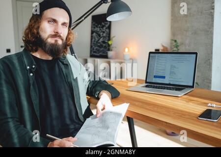 Young beard college student sit by the work table and prepare to pass exam to university. University student studying and making notes at campus. Stock Photo