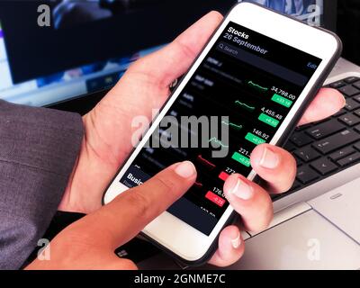 Online trading and stock broker concept backdrop with young man holding mobile. Stock Photo
