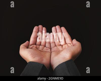 Young man raising hands for prayer in the air. Modern prayer style with dark background Stock Photo