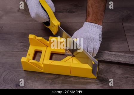 A man cuts the skirting board using a saw and miter box on laminate floor. Stock Photo